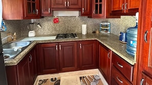 A kitchen with dark wooden cabinets, granite countertops, a built-in stove, and a large water dispenser.