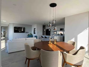 Uma sala de estar moderna com uma mesa de jantar redonda de madeira, cadeiras estofadas brancas e um sofá branco.