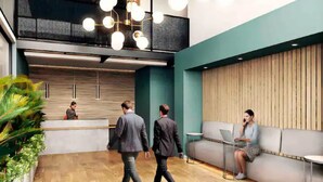 Un área de recepción moderna con un mostrador de madera, una zona de estar con un sofá y una mesa, y una escalera que conduce a un nivel superior.
