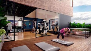 Un área de gimnasio al aire libre con equipo de ejercicio, una terraza de madera y vistas de la ciudad.