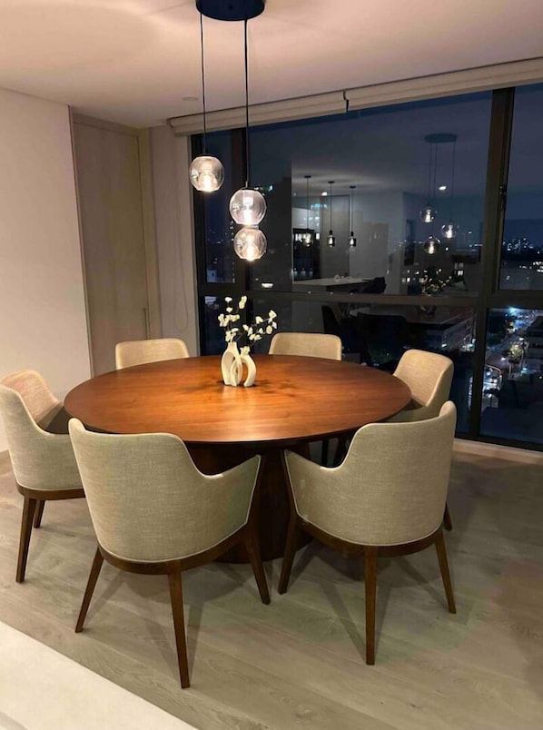 Uma área de refeições moderna com uma mesa redonda de madeira, seis cadeiras estofadas e um vaso com flores.
