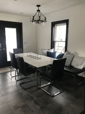 Uma sala de jantar moderna com uma mesa retangular, cadeiras pretas, um candelabro e um banco com almofadas.