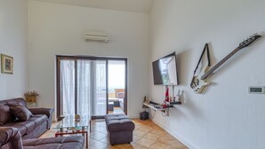 A living room with a sofa, ottoman, and a glass coffee table. There is a TV mounted on the wall and a guitar hanging on the wall. - Pool House Kristina near Poreč, Kaštelir - Labinci, Croatia (Kaštelir - Labinci)