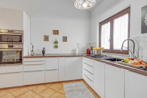 Een moderne keuken met witte kastjes, een ingebouwde oven, een spoelbak en een raam met gordijnen.
