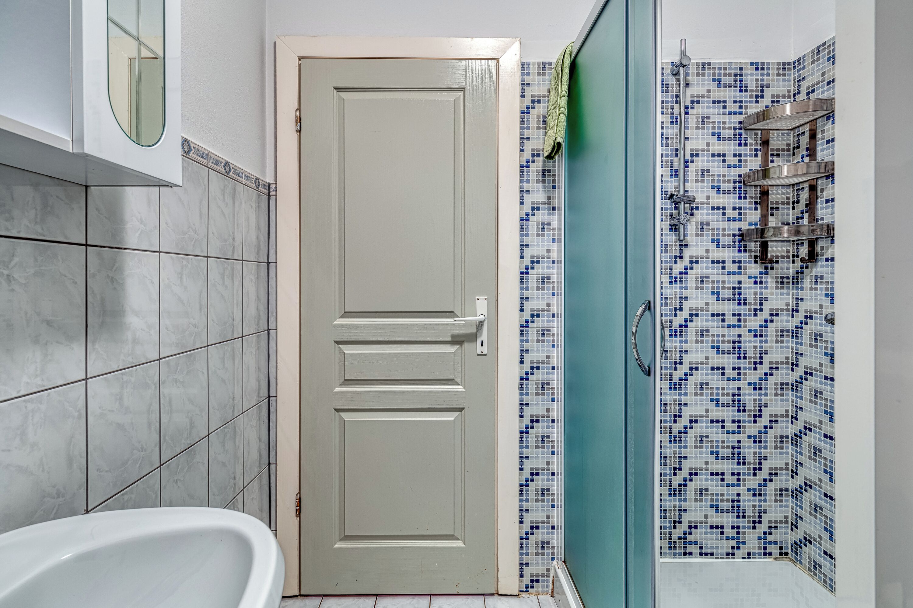 A bathroom with a white bathtub, a door, and a shower area with blue mosaic tiles.