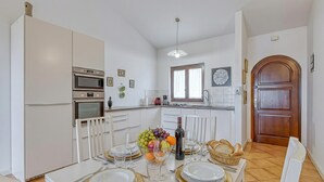 A modern kitchen with white cabinets, a dining table set for four with gold accents, and a fruit bowl on the table. - Pool House Kristina near Poreč, Kaštelir - Labinci, Croatia (Kaštelir - Labinci)