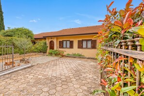 A house with a tiled roof, a paved hexagonal courtyard, and a variety of plants.