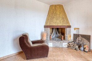 Een gezellige kamer met een stenen openhaard, een bruine fauteuil en een betegelde vloer.