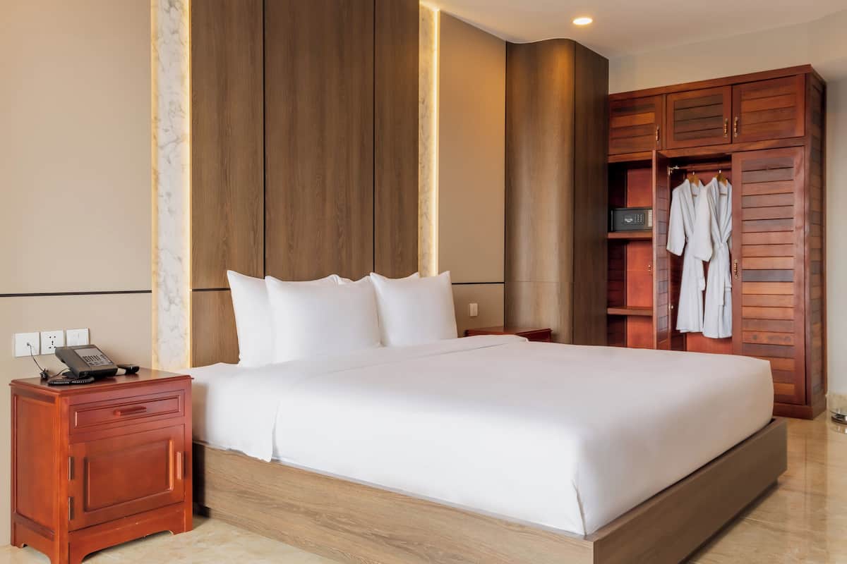 Un lit bien fait dans une chambre d’hôtel, avec une armoire en bois et une table de chevet sur laquelle se trouve un téléphone.