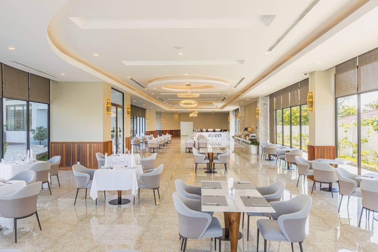 A spacious, well-lit dining area with multiple tables and chairs, large windows, and a modern ceiling design.