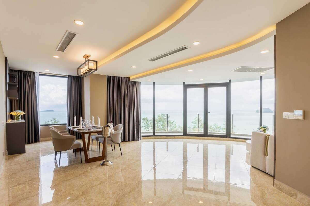 Une chambre d’hôtel moderne avec une grande fenêtre, un coin repas avec une table dressée, et un sol propre et ciré.