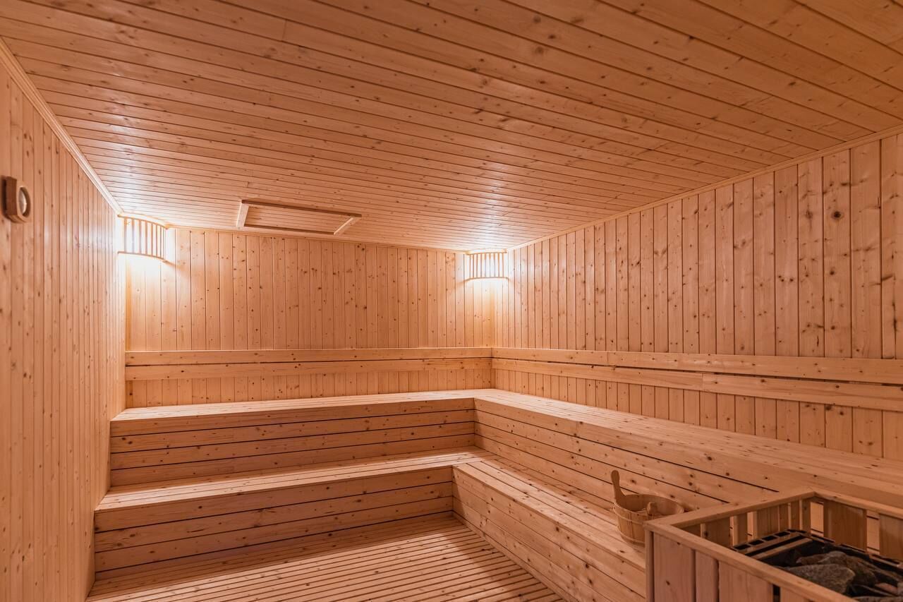 A wooden sauna with benches and a bench seat, a wooden floor, and two wall-mounted lights.