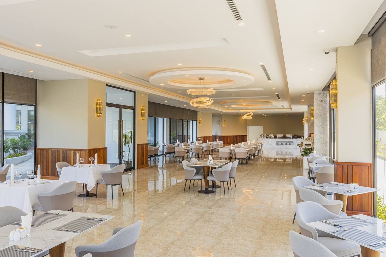 A spacious restaurant with multiple dining areas, large windows, and modern chandeliers.