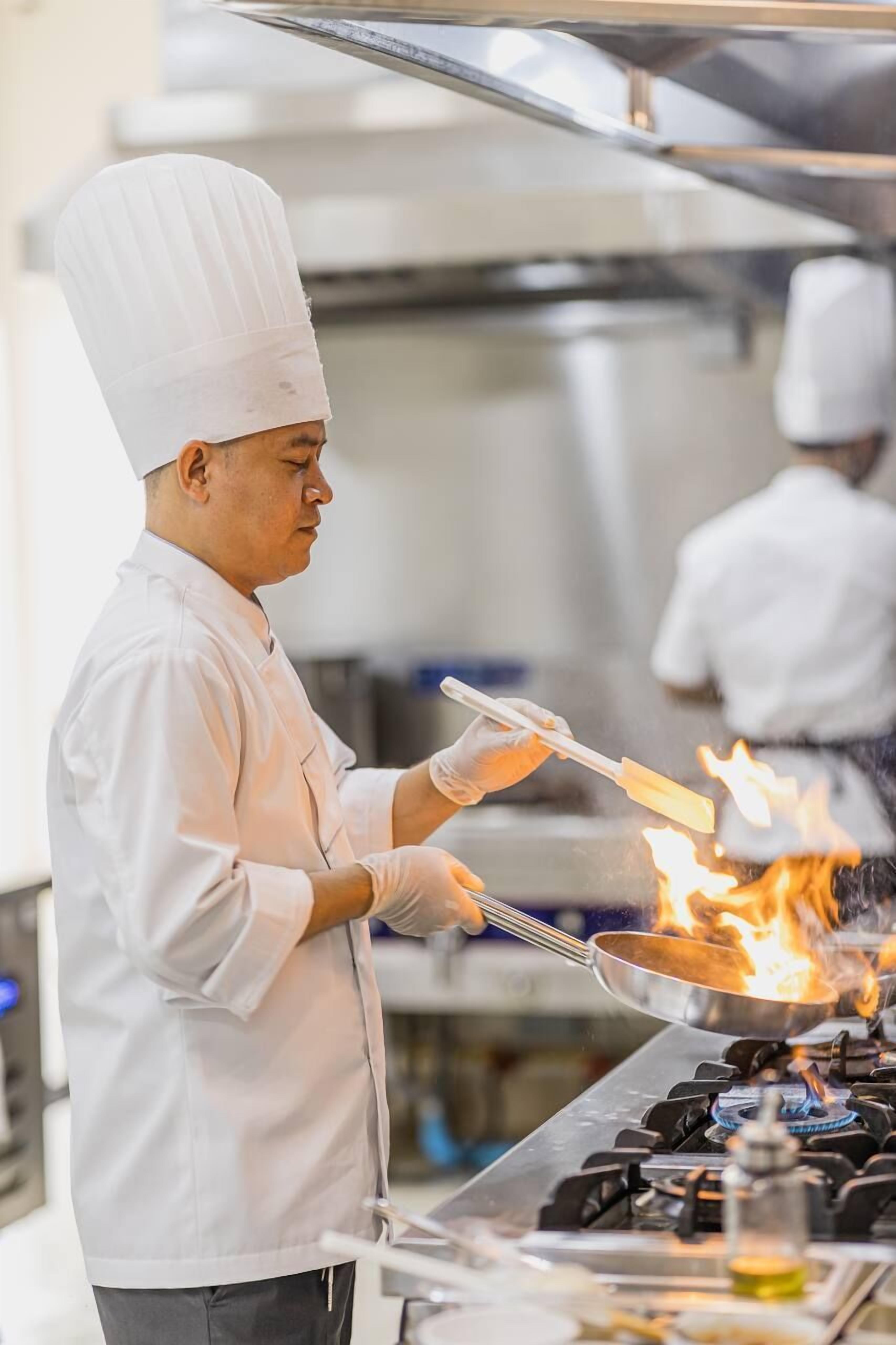 A chef cooking with a pan on a stove.
