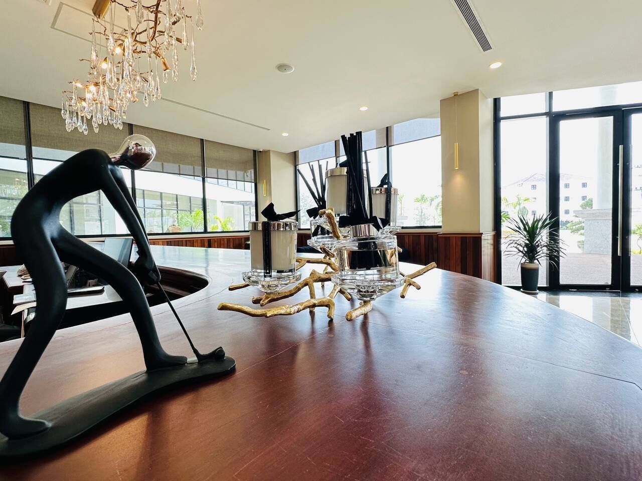 A spacious lobby with a large wooden table, a modern chandelier, and large windows offering a view of the city.