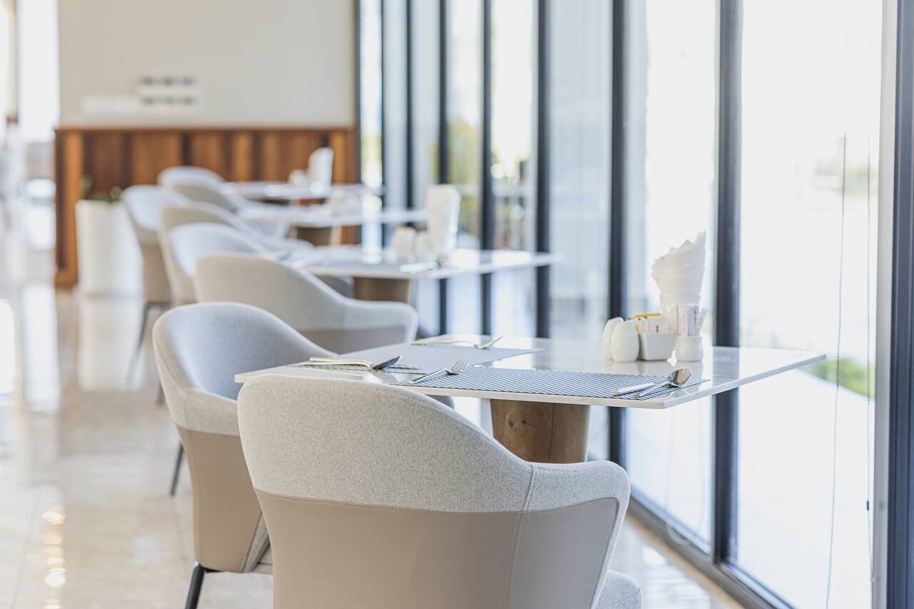 Un comedor moderno con mesas y sillas, ventanas amplias y un diseño limpio y minimalista.