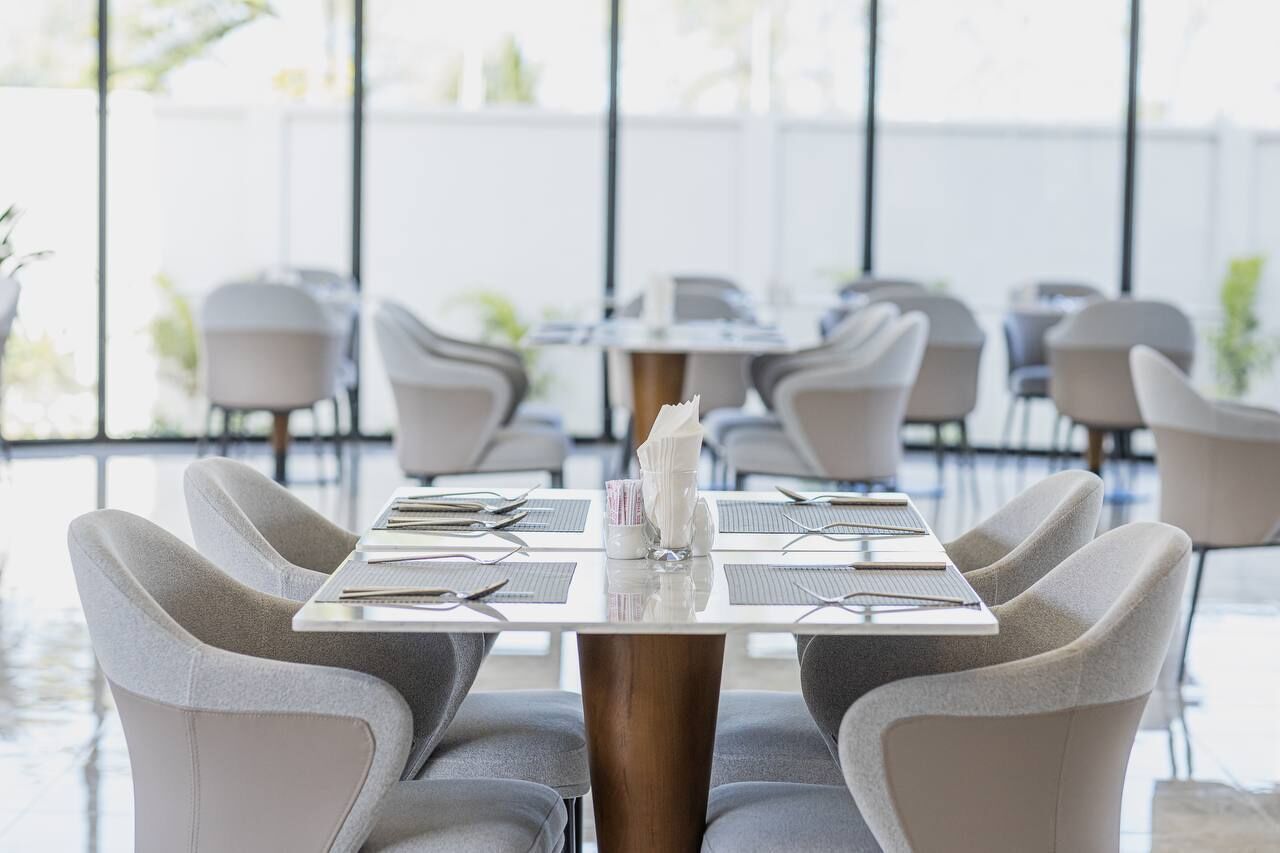 A modern dining area with a table set for four, surrounded by chairs, in a bright room with large windows.