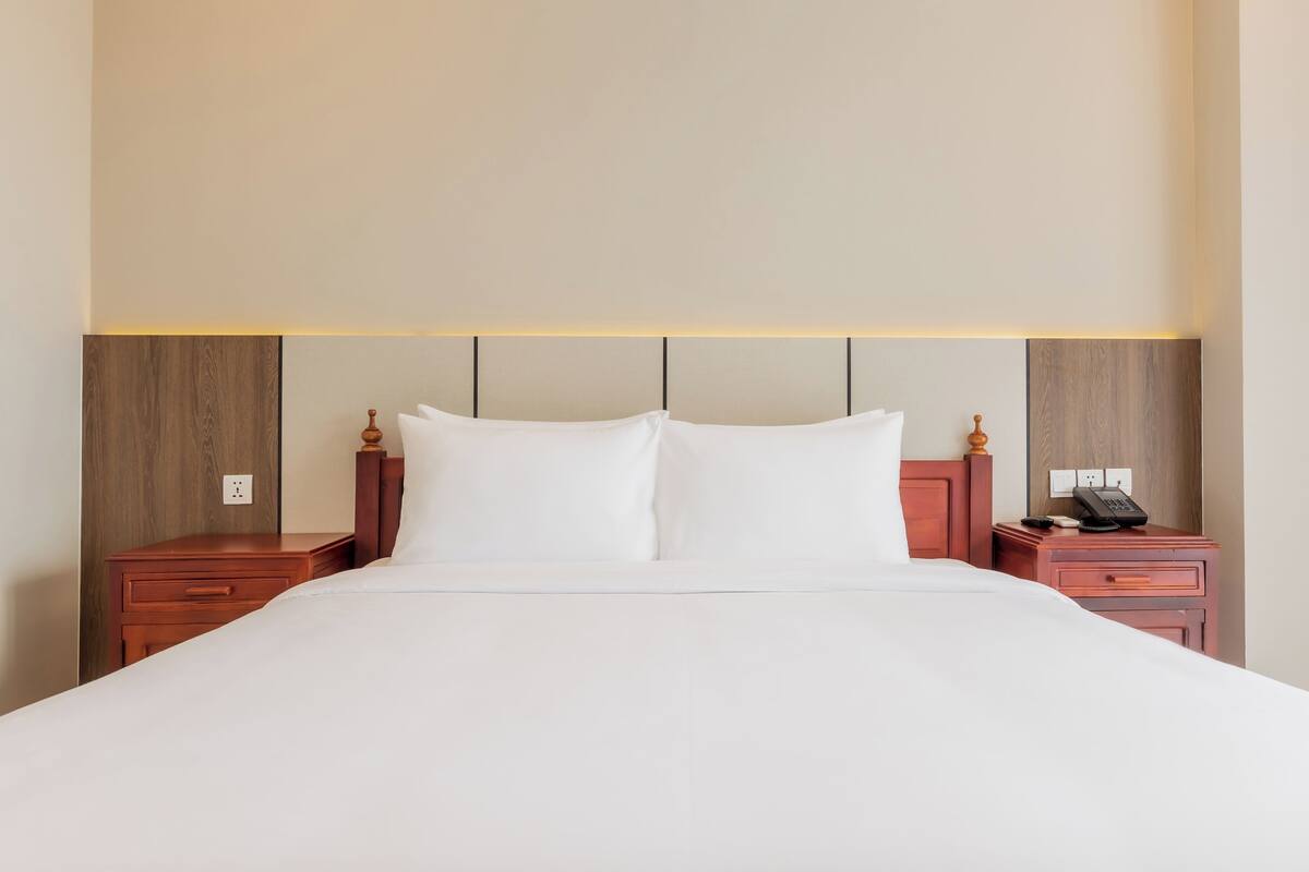 Une chambre d’hôtel avec un grand lit, deux tables de chevet en bois, un téléphone et une prise électrique murale.