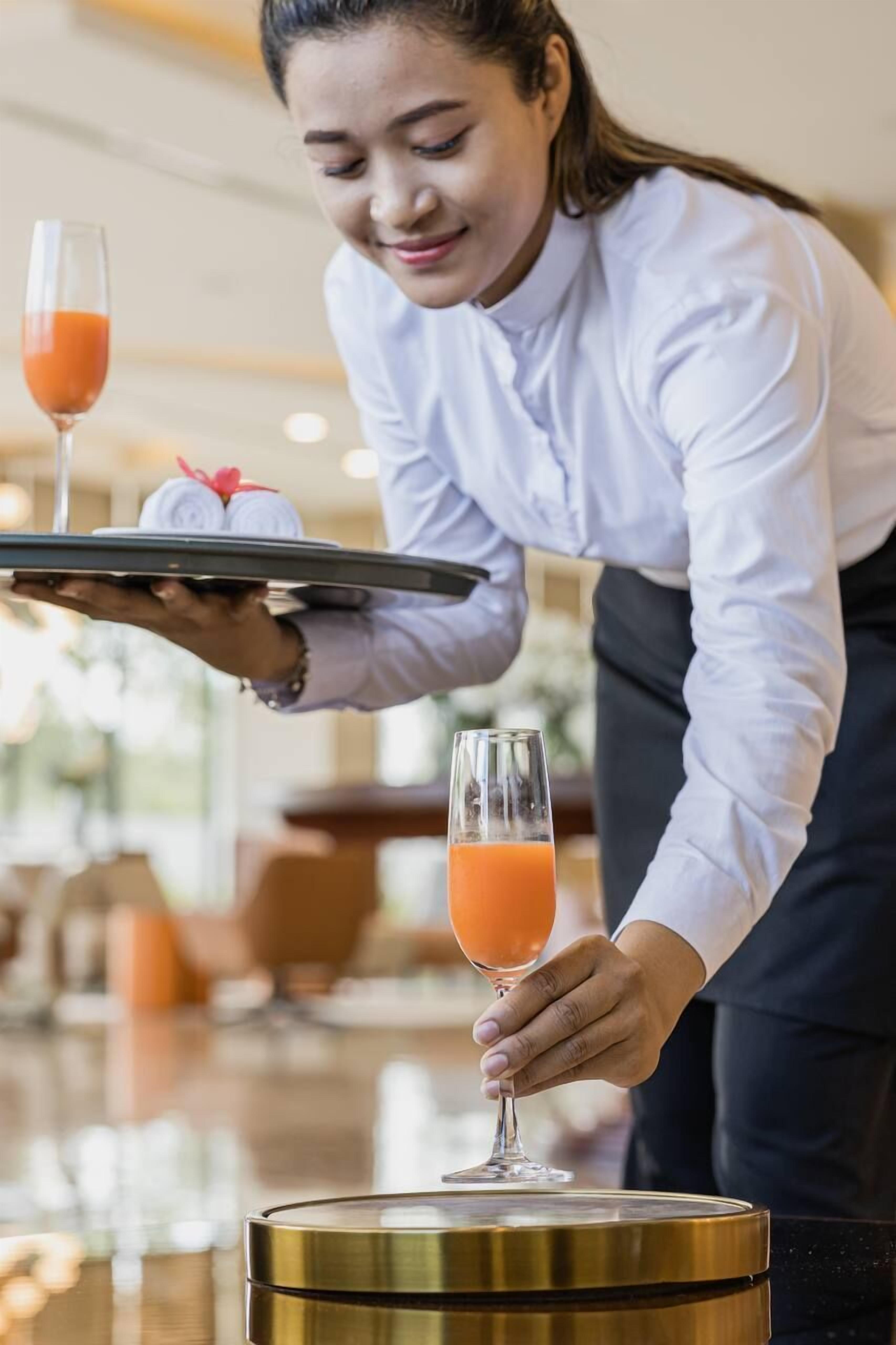 A person serving a glass of orange juice and a rolled towel on a tray.