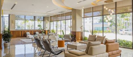 A spacious lobby with a modern design, featuring a seating area with sofas and chairs, large windows offering views of the outside, and a polished marble floor.