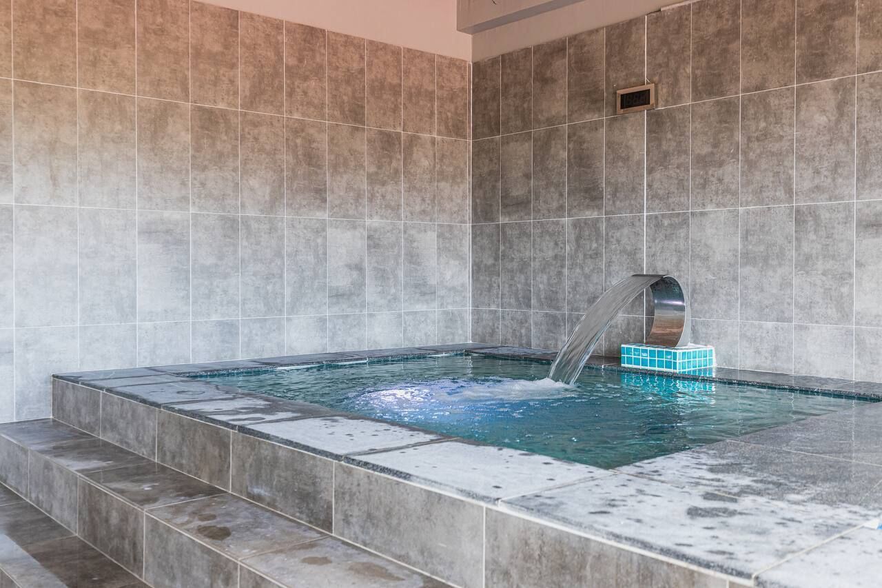 Zona de spa con hidromasaje, paredes con azulejos y una ventana pequeña.