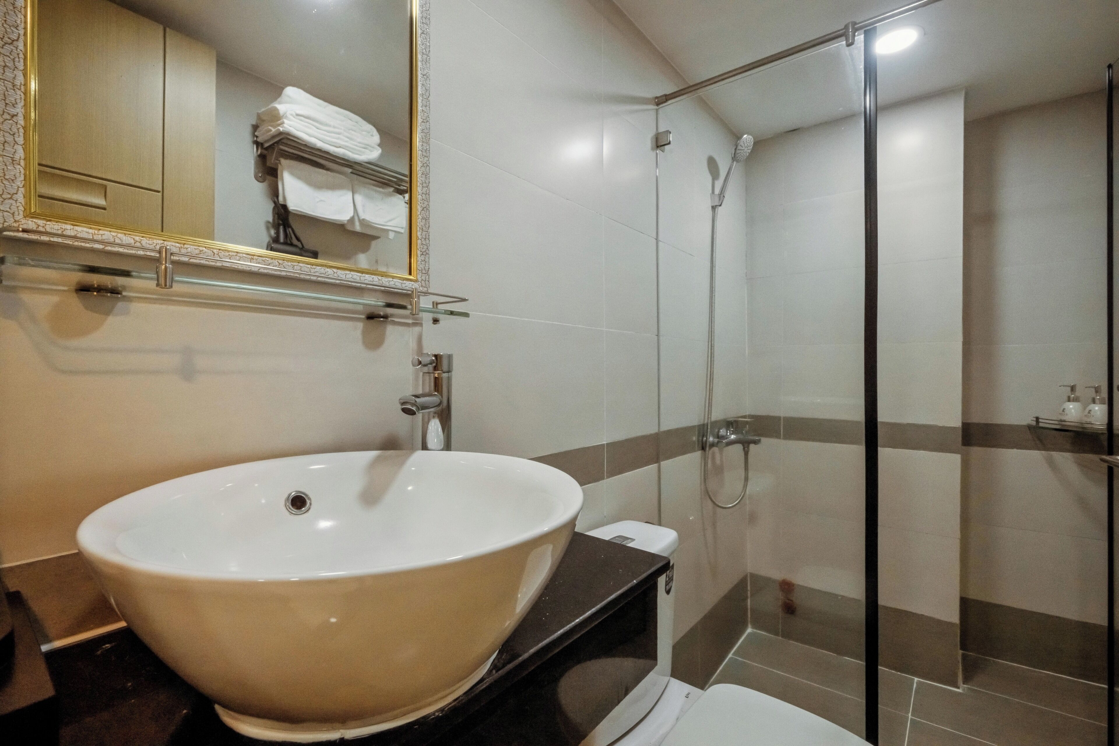 Un baño con un lavamanos grande de color blanco, un box de ducha de vidrio y un espejo con marco dorado.