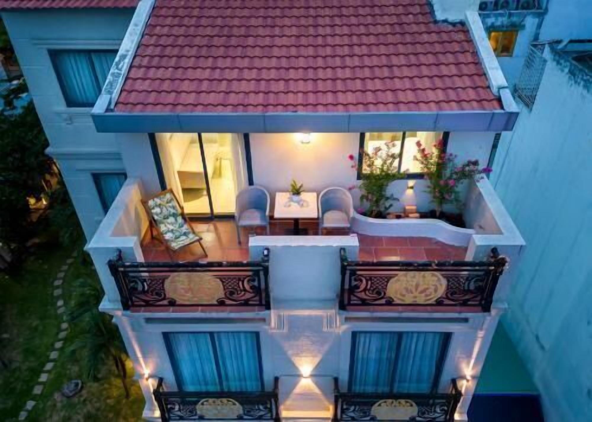 Un edificio de dos pisos con balcón, mobiliario exterior y vista a un jardín.
