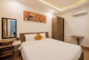 A hotel room with a bed, a desk, a chair, a painting, and an air conditioning unit. - Kelly Hotel SECC Phu My Hung (Ho Chi Minh City)