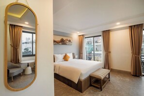Une chambre d’hôtel avec un lit, une banquette, une petite table, une chaise et un grand miroir.