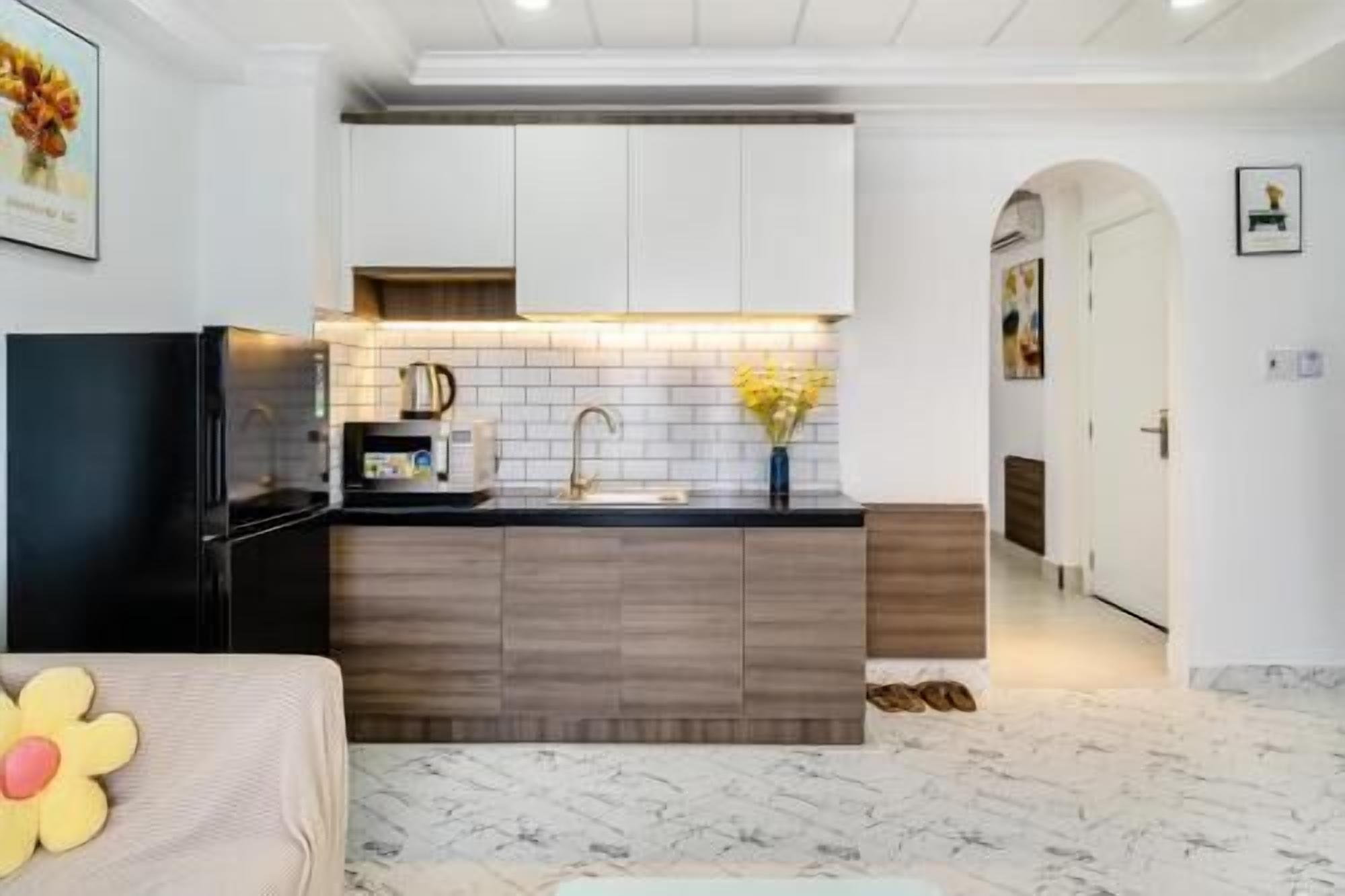 A modern kitchen with a black refrigerator, wooden cabinets, and a marble floor.