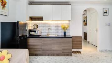 A modern kitchen with a black refrigerator, wooden cabinets, and a marble floor.
