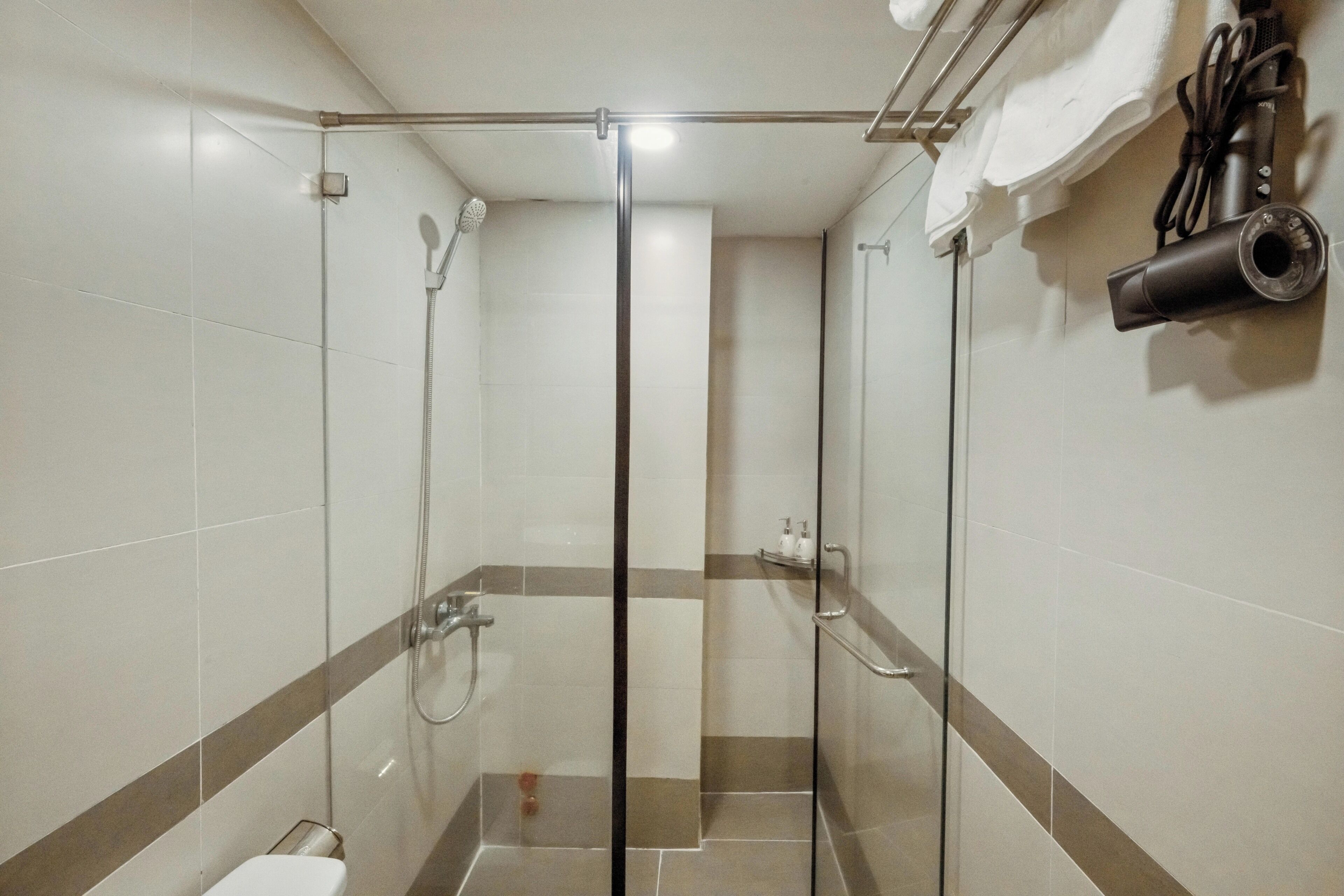 A glass-enclosed shower stall with a handheld showerhead, a towel rack, and a toilet.