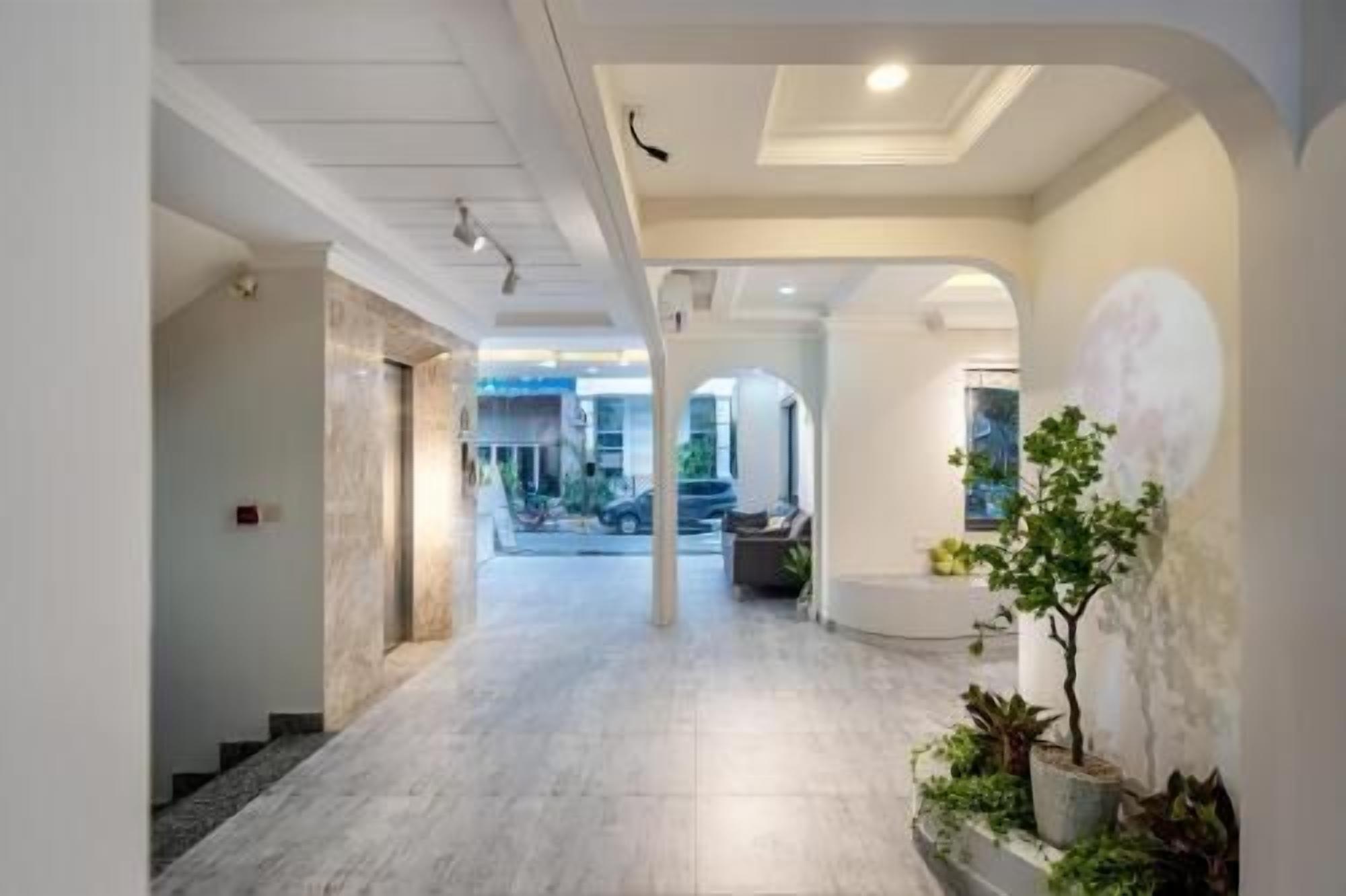 A hallway with a marble floor, white walls, and a plant on the right. There are columns and a ceiling light.