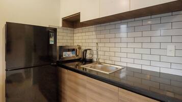 Cocina con refrigerador negro, pileta de acero inoxidable y salpicadero de azulejos blancos.