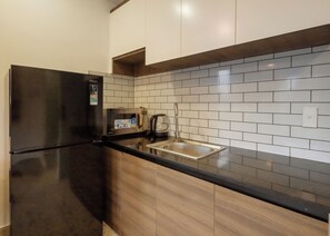 A kitchen with a black refrigerator, a stainless steel sink, and white tiled backsplash. - Kelly Hotel SECC Phu My Hung (Ho Chi Minh City)