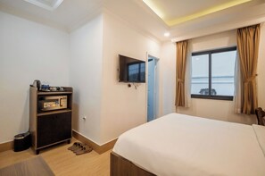 A hotel room with a bed, a TV mounted on the wall, a small shelf with toiletries, and a window with curtains. - Kelly Hotel SECC Phu My Hung (Ho Chi Minh City)