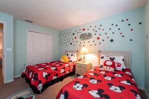 A bedroom with two beds, each covered in red bedding with Mickey Mouse prints. There is a nightstand with a lamp between the beds, and a wall decorated with Mickey Mouse and Minnie Mouse stickers. - Near to Disney/ Large Yard/ Private pool/ Quiet Community (Davenport)