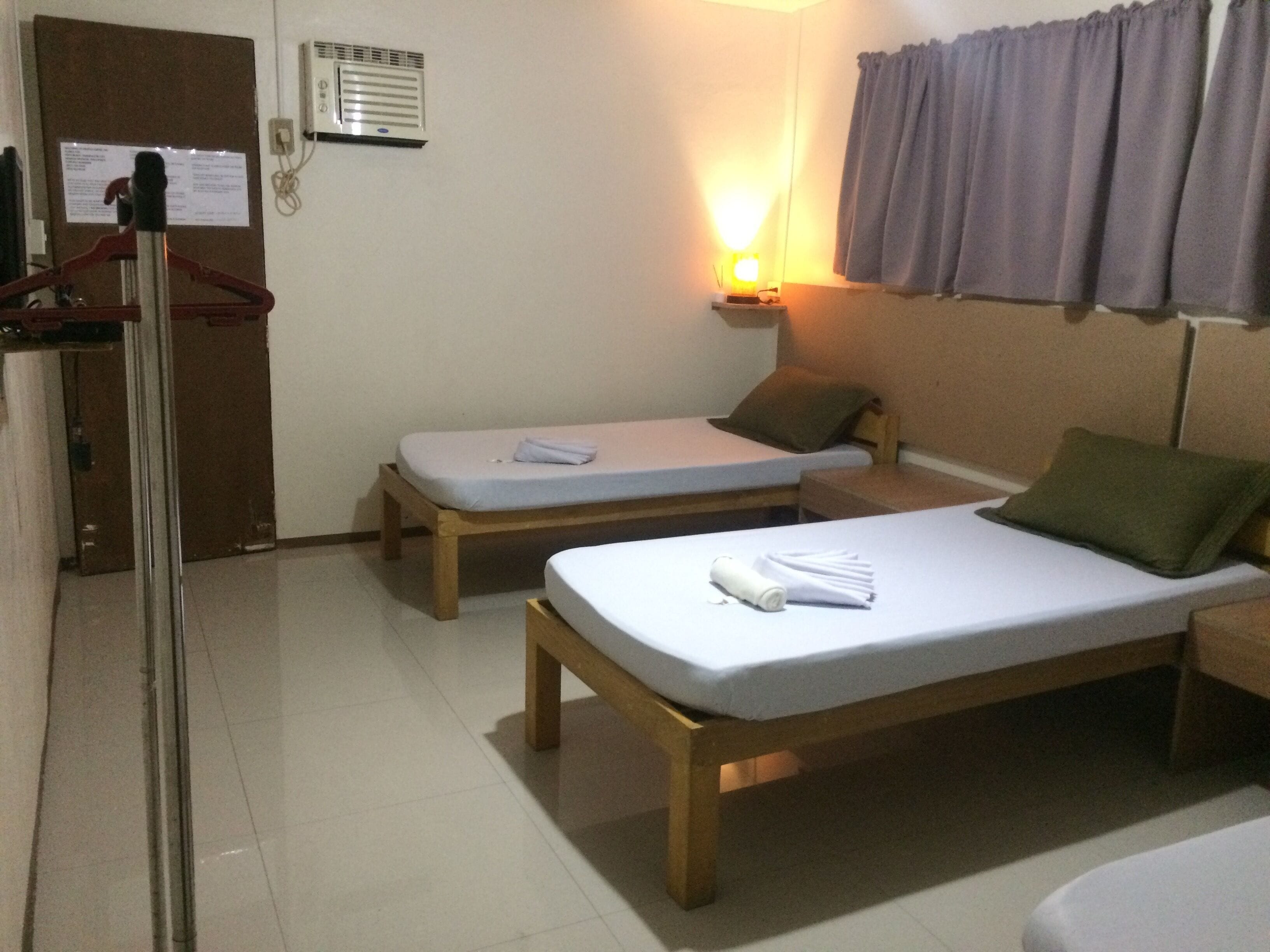 A room with two single beds, a wooden bench, a small table with a lamp, and a door with a coat rack.