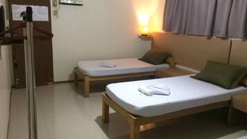 A room with two single beds, a wooden bench, a small table with a lamp, and a door with a coat rack.
