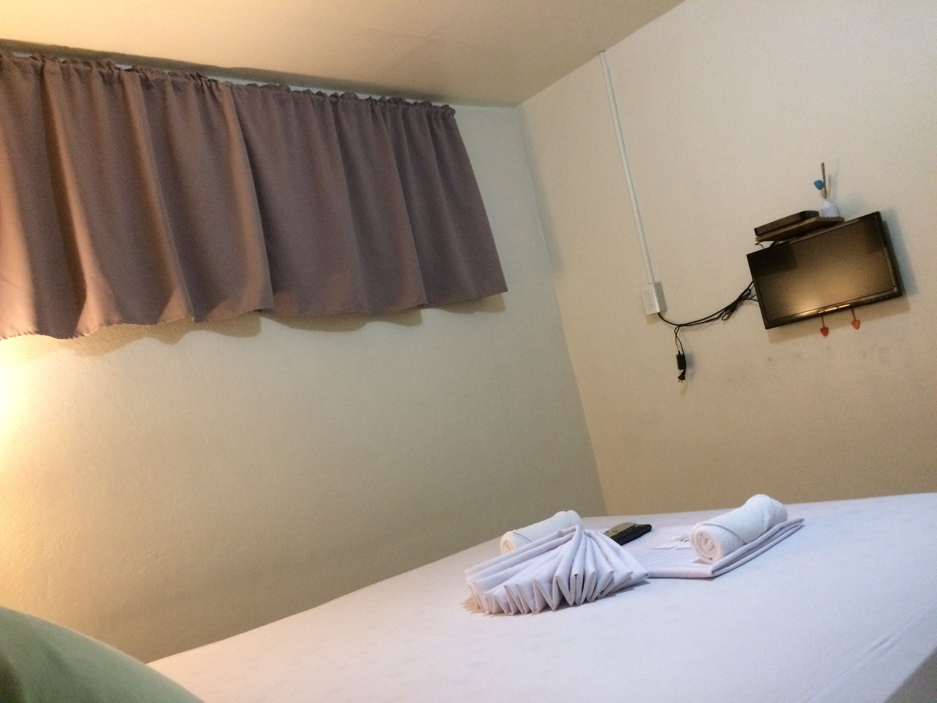 A hotel room with a bed, a wall-mounted TV, and a power outlet.