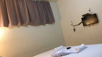 A hotel room with a bed, a wall-mounted TV, and a power outlet.