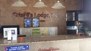 A reception area with a sign reading "CrisFit's Lodge, Inc." and a year "1969" below it. There are framed signs on the wall, a counter with a sign that says "Please Stand Behind This Line," and a chalkboard with "Coffee & Water" written on it. - CRISFILS LODGE INCORPORATED (Dumaguete)
