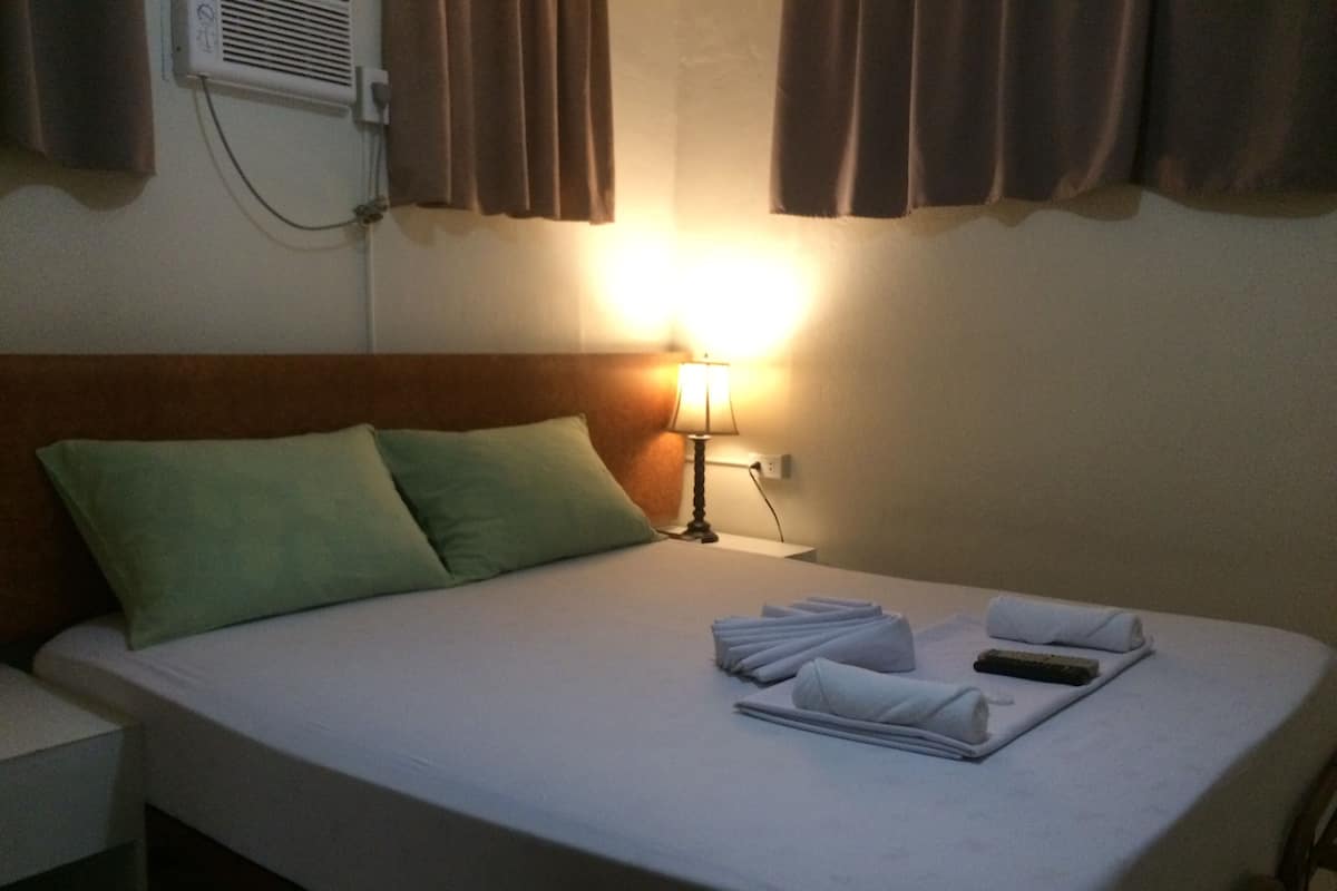 Quarto de hotel com cama bem arrumada, almofadas, abajur e toalha dobrada na cama.