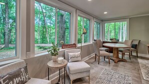 A spacious room with large windows, a round wooden table, and comfortable seating. - The Farm House (Blythewood)