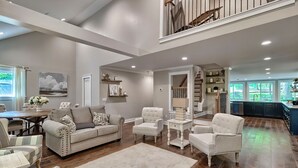 A spacious living room with a high ceiling, a dining area, and a kitchen visible through an open doorway. - The Farm House (Blythewood)
