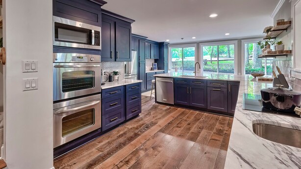 A modern kitchen with dark blue cabinets, stainless steel appliances, and a wooden floor. - The Farm House (Blythewood)