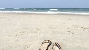 Una spiaggia con un paio di ciabatte sulla sabbia, onde sullo sfondo e cielo sereno.