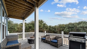 Una terrazza coperta con mobili in vimini, un barbecue e vista sugli alberi.