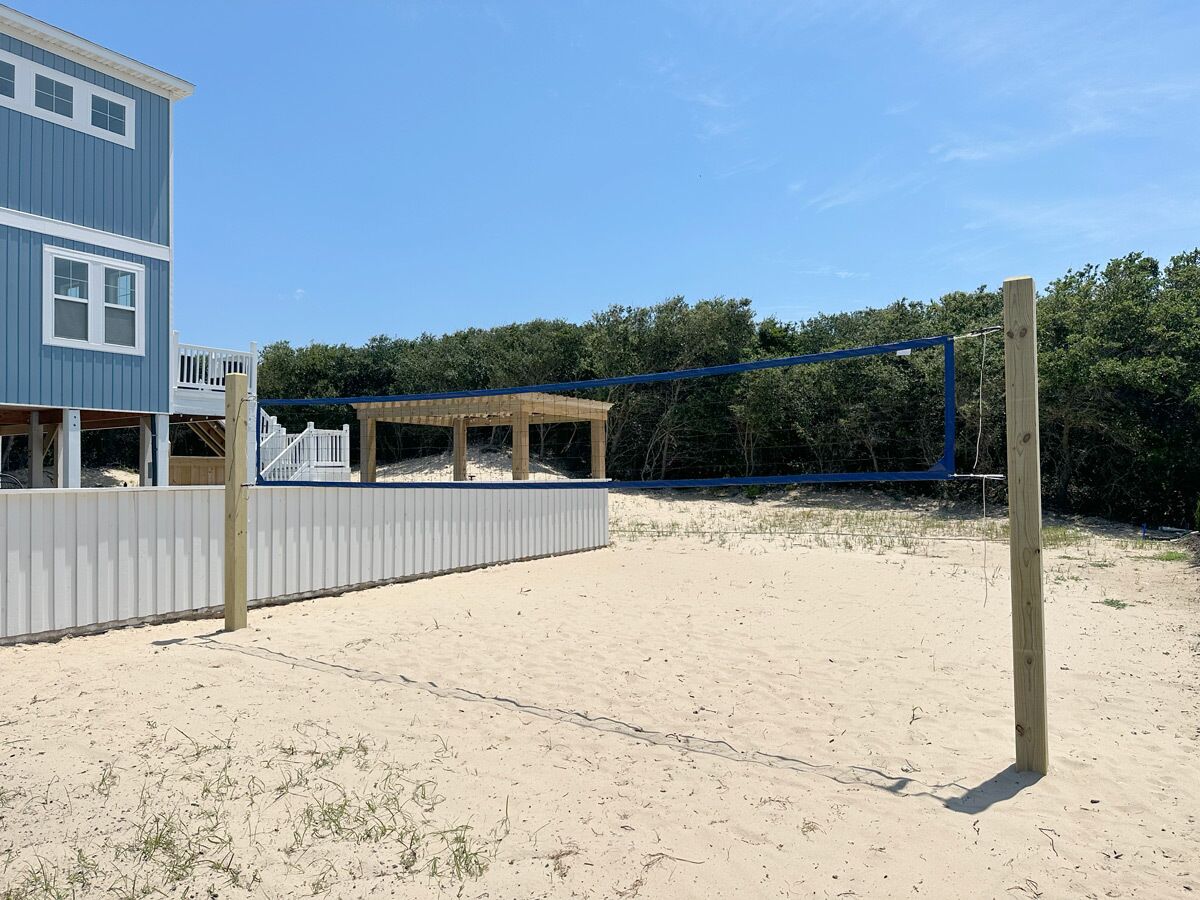 A beach with a wooden fence, a blue structure, and a building with a balcony.