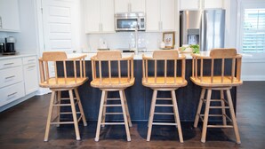 A modern kitchen with white cabinets, stainless steel appliances, and wooden bar stools. - The Teal Door Cottage-Spacious home with King suite (Nashville)